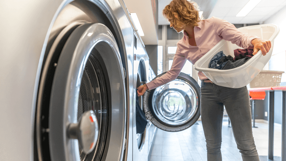 Mulher em lavanderia self-service retirando roupas da máquina de lavar